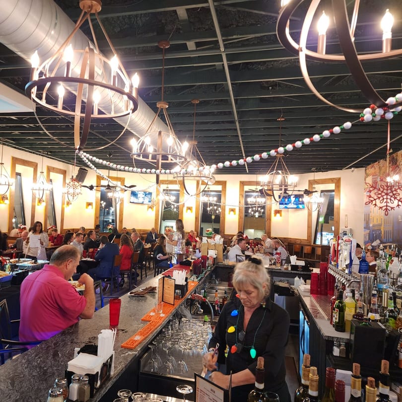 A lively Portofino's Italian restaurant interior with patrons dining and a bartender working.