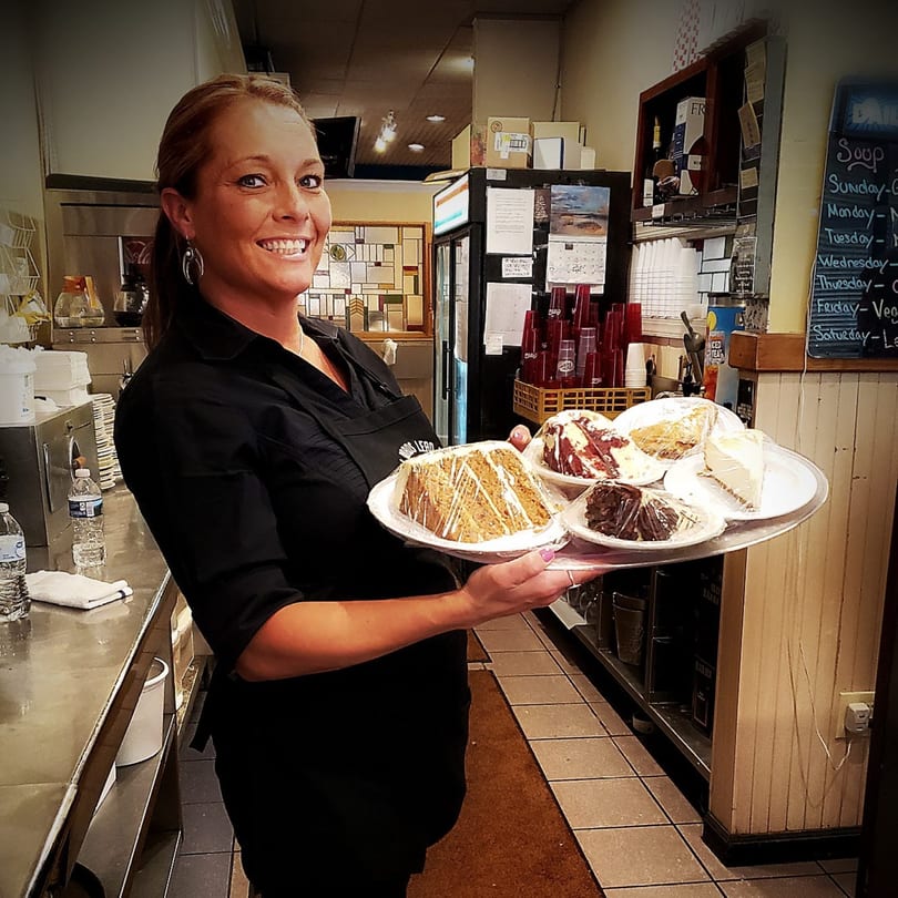 A smiling Portofino's waitress holds a tray with four slices of cake, ready to serve.