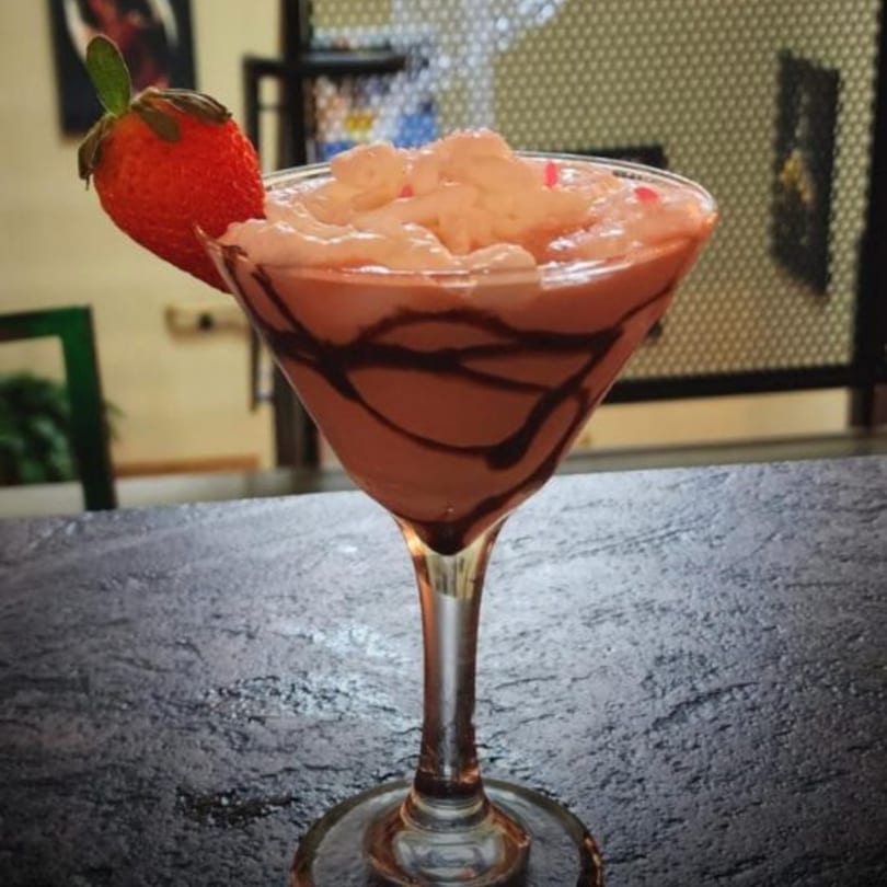 A strawberry martini with chocolate drizzle and whipped topping, garnished with a fresh strawberry.