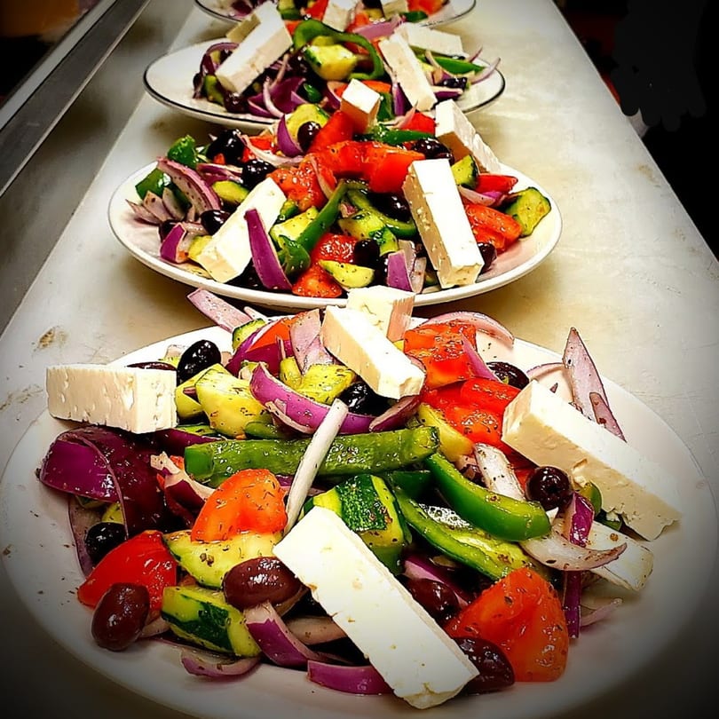 Multiple plates of fresh Greek salad with cucumbers, tomatoes, red onions, olives, and feta cheese.