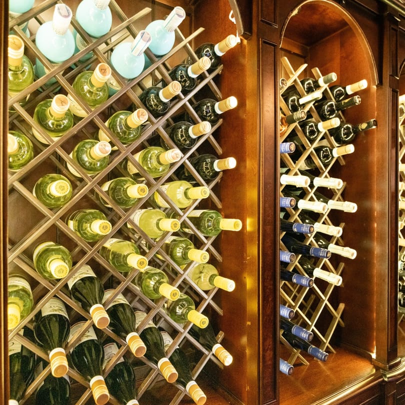 Wine bottles, both white and red, stored in wooden racks within a dark wooden cabinet.