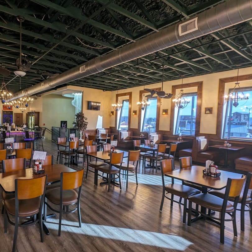 Spacious dining room at Portofino's with tables, chairs, booths, and a bar area under a dark ceiling.