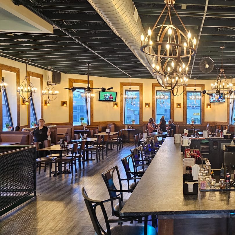 Interior of Portofino's Italian restaurant with dining tables, booths, a bar, and chandeliers.