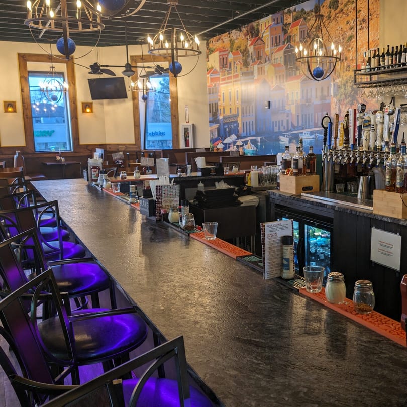 Portofino's bar area with purple-lit stools, a mural of a Mediterranean village, and beer taps.