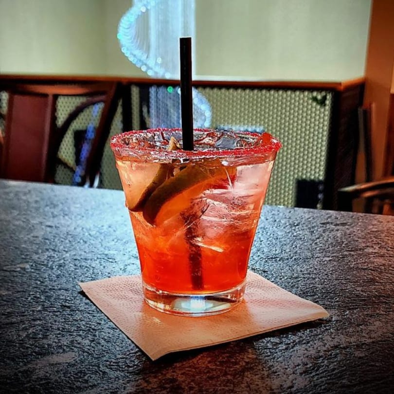A vibrant red cocktail with a sugared rim and lime wedges sits on a napkin at Portofino's.