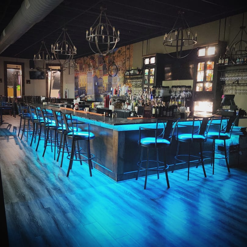 Portofino's bar with blue under-lighting, bar stools, and a mural of an Italian village.