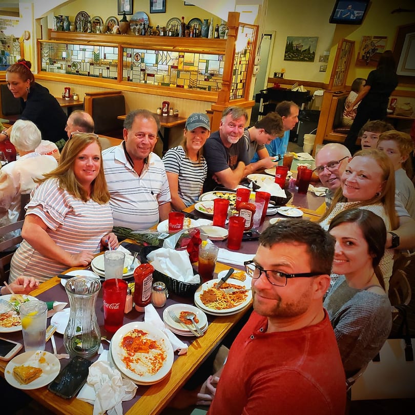 A large group of people smiling and dining together at Portofino's Greek and Italian Restaurant.
