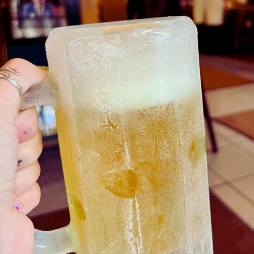 A hand holds a frosty mug filled with a golden beer and a foamy head.