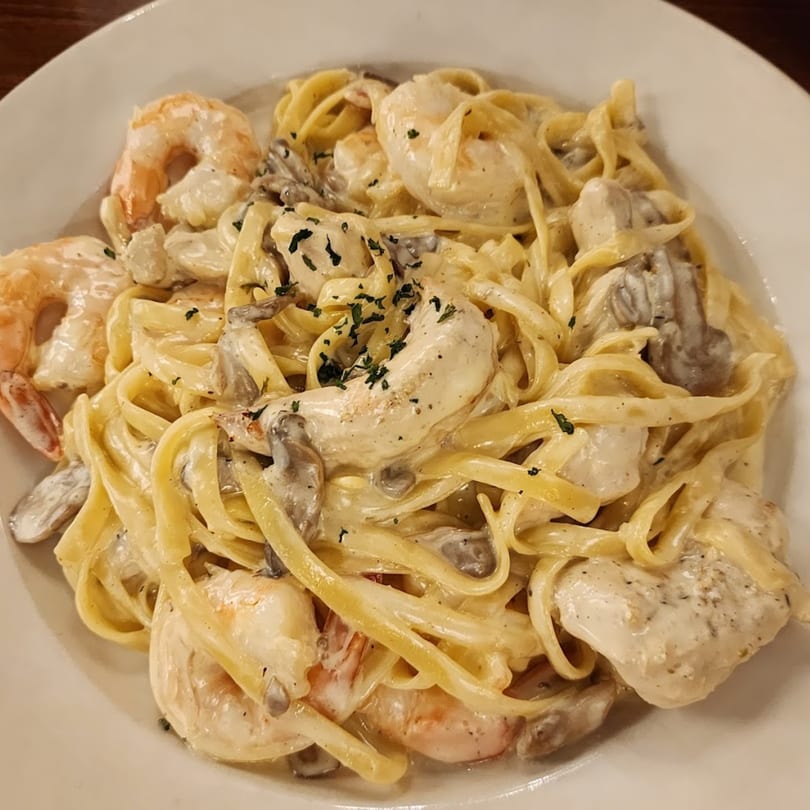 Creamy Portofino's Italian fettuccine pasta with shrimp, chicken, and mushrooms, garnished with parsley.