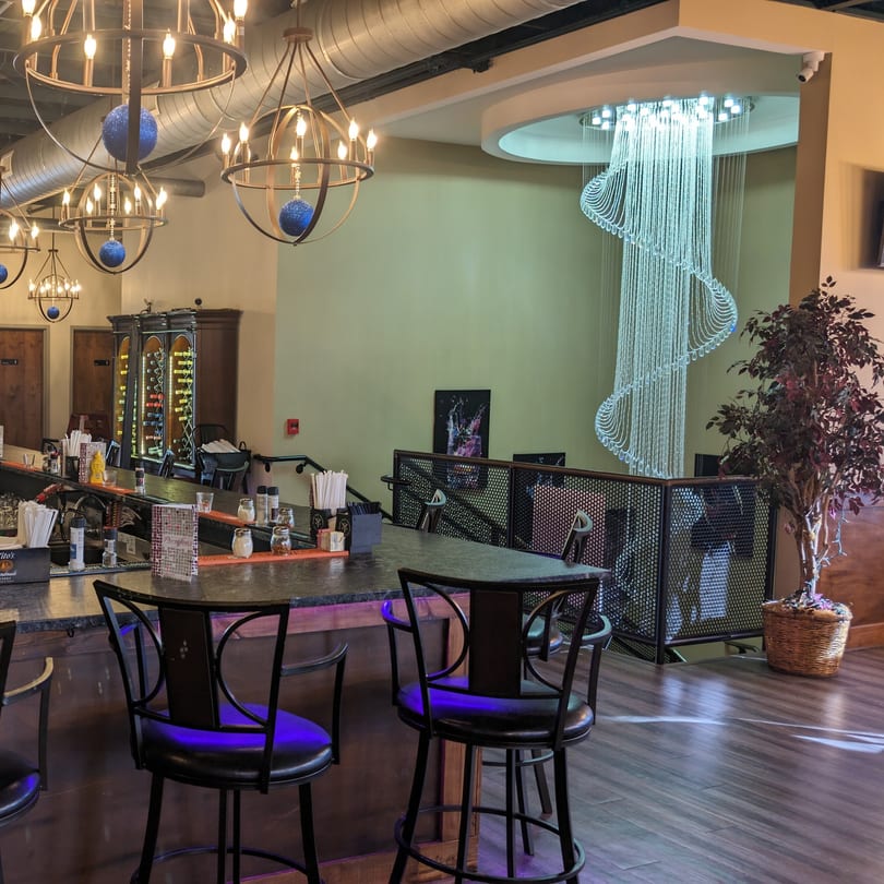 A bar area with ornate chandeliers, a spiral crystal light fixture, and wine racks.